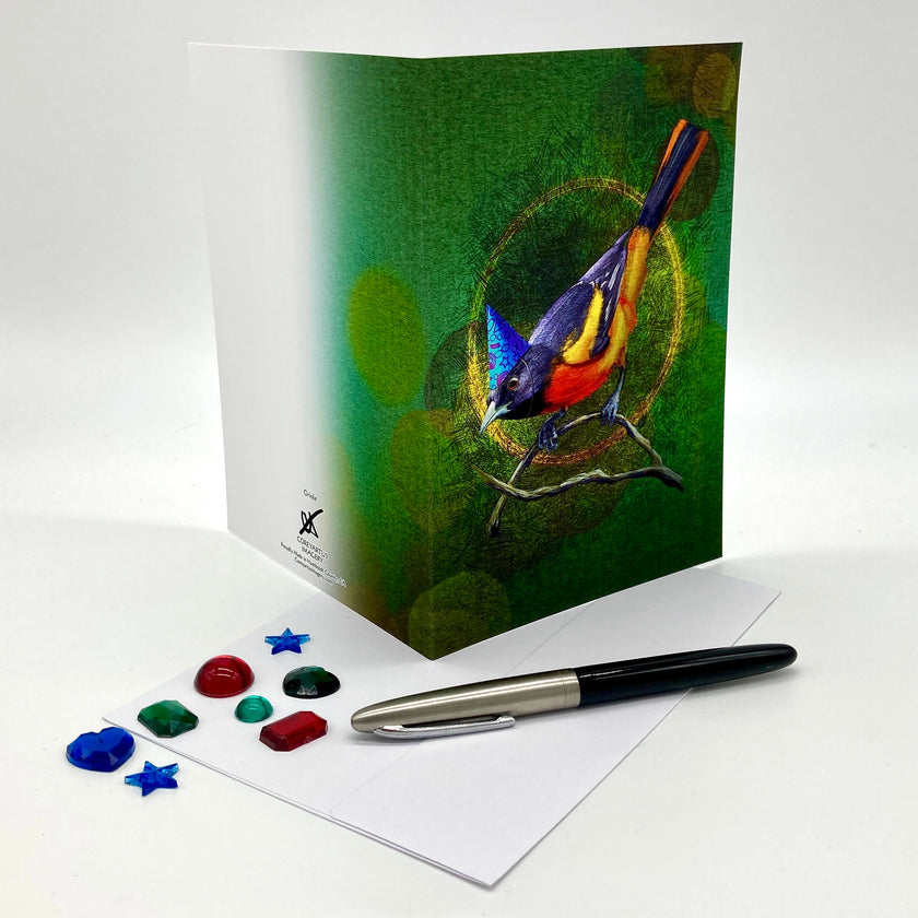Greeting card with a colorful bird illustration on a green background, accompanied by a pen and decorative stones.