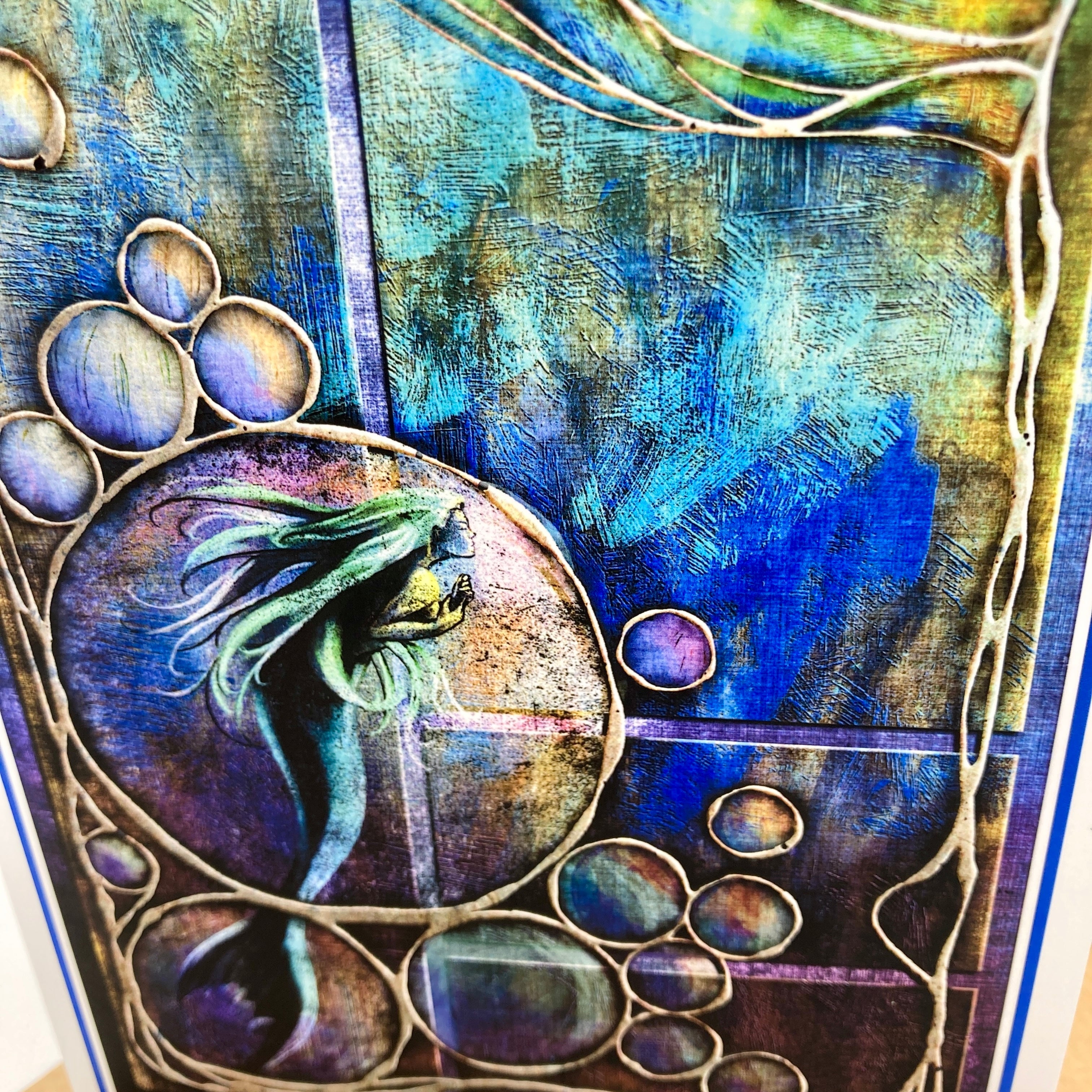 An abstract mixed-media artwork featuring a stylized mermaid inside a circular frame, surrounded by organic bubble-like shapes and flowing vine-like lines in deep blue, teal, purple, and gold tones.