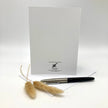 Back side of a greeting card, posed with a sprig of wild grass and a writing pen on a paper envelope.