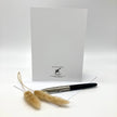 Backside of a greeting card, posed with a spring of wild grasses and a black ink pen on a white envelope against a white background.