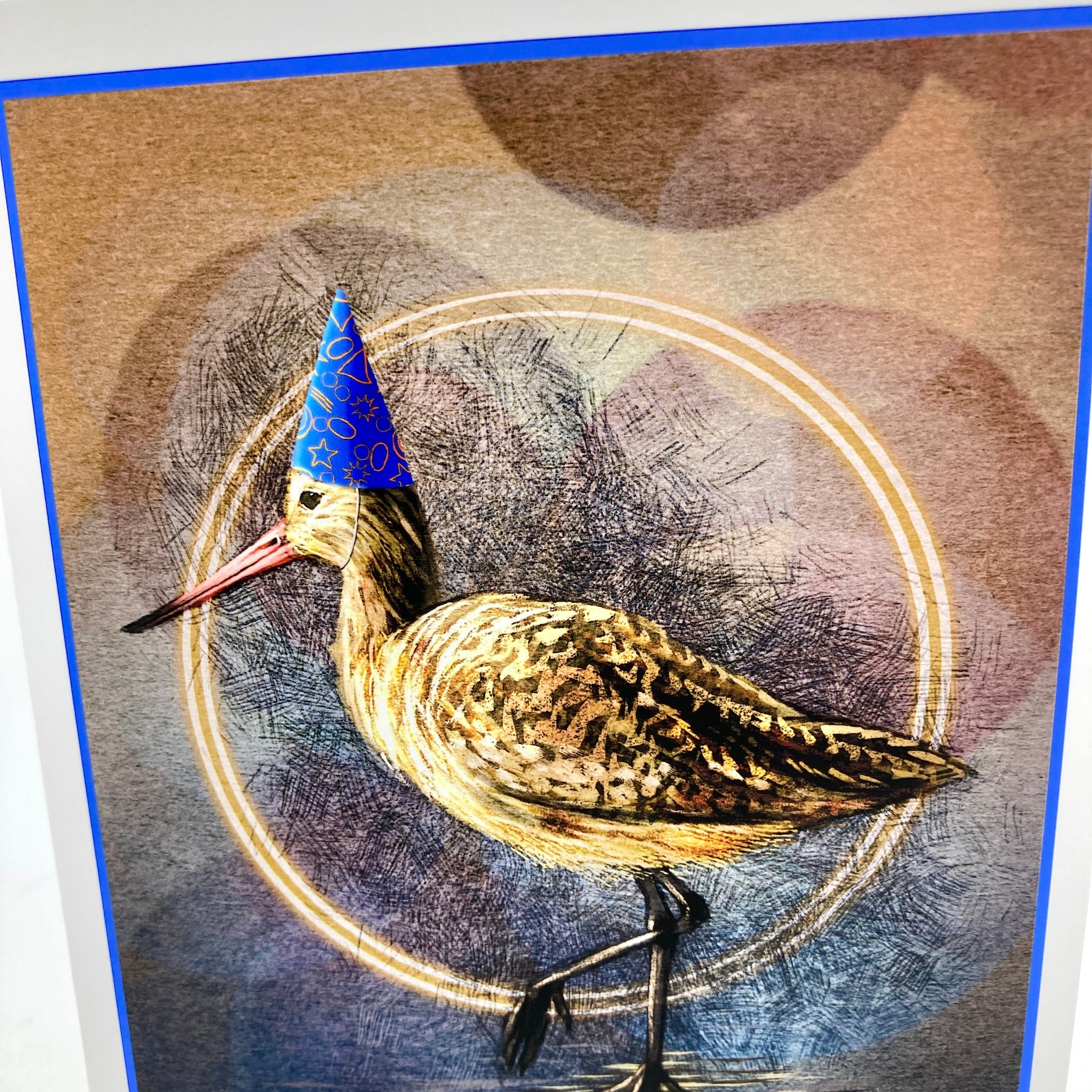 Closeup of a birthday card featuring a marbled Godwit in a blue party hat.