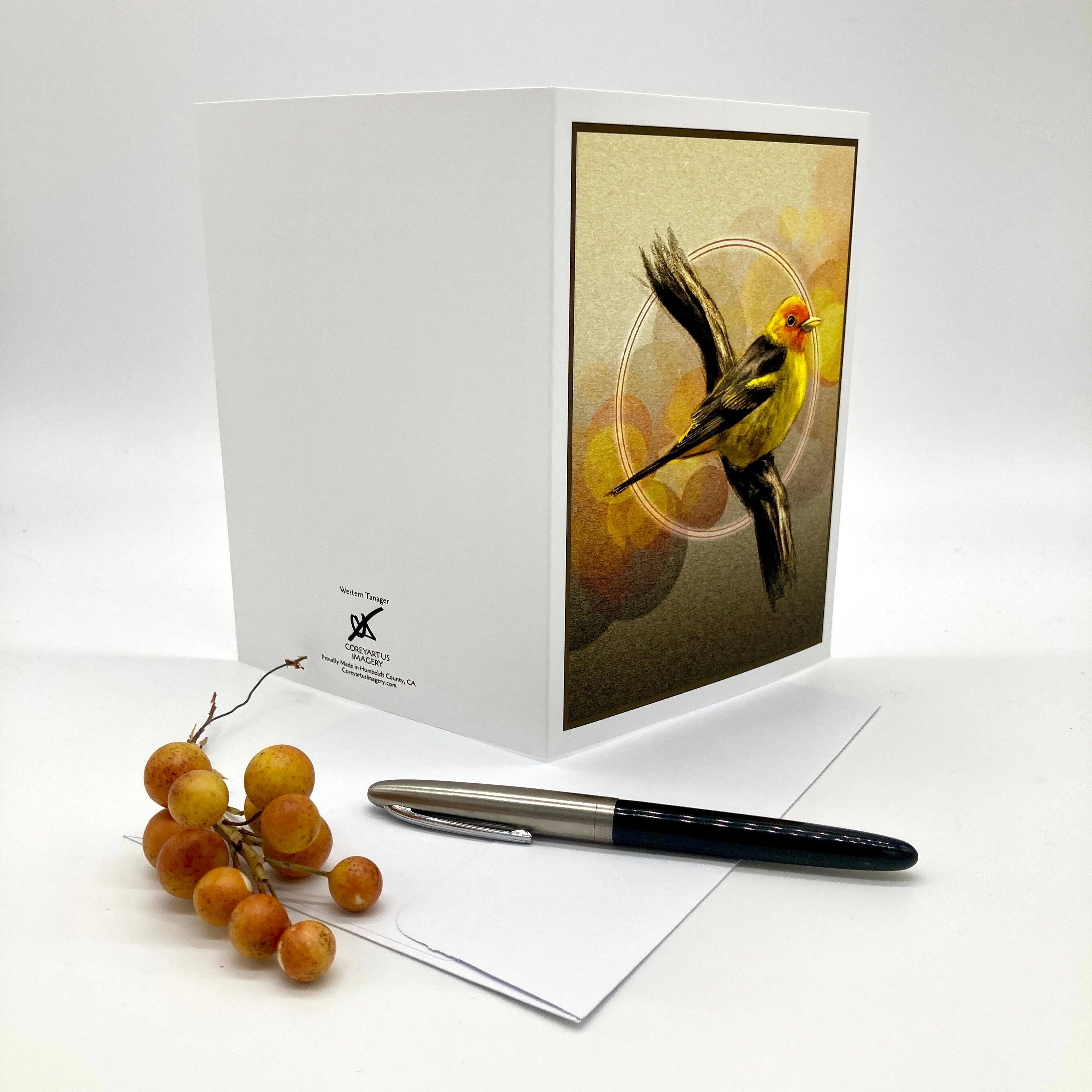 A white greeting card with a printed illustration of a yellow bird on the front, displayed with an envelope and a black pen on a white background. The card shows the brand name 'The Art of X' printed near the bottom left.