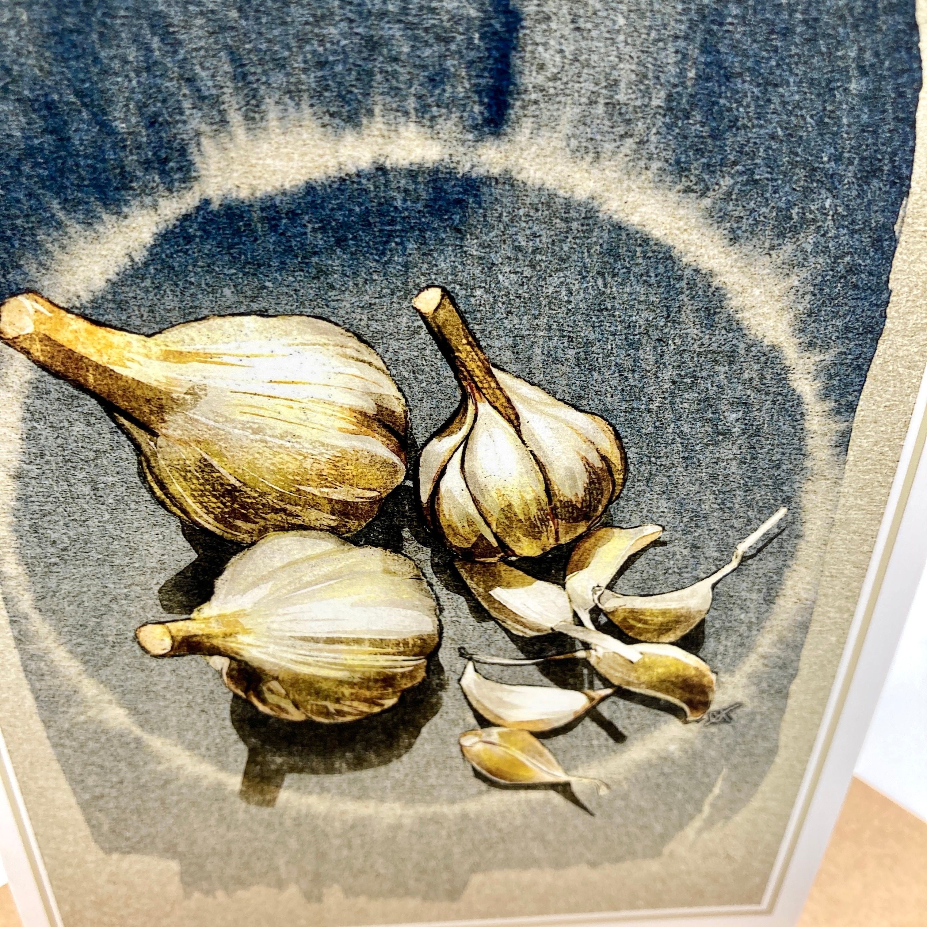 A framed still life art print depicting garlic bulbs and cloves rendered in muted blue-gray, beige, and brown tones.