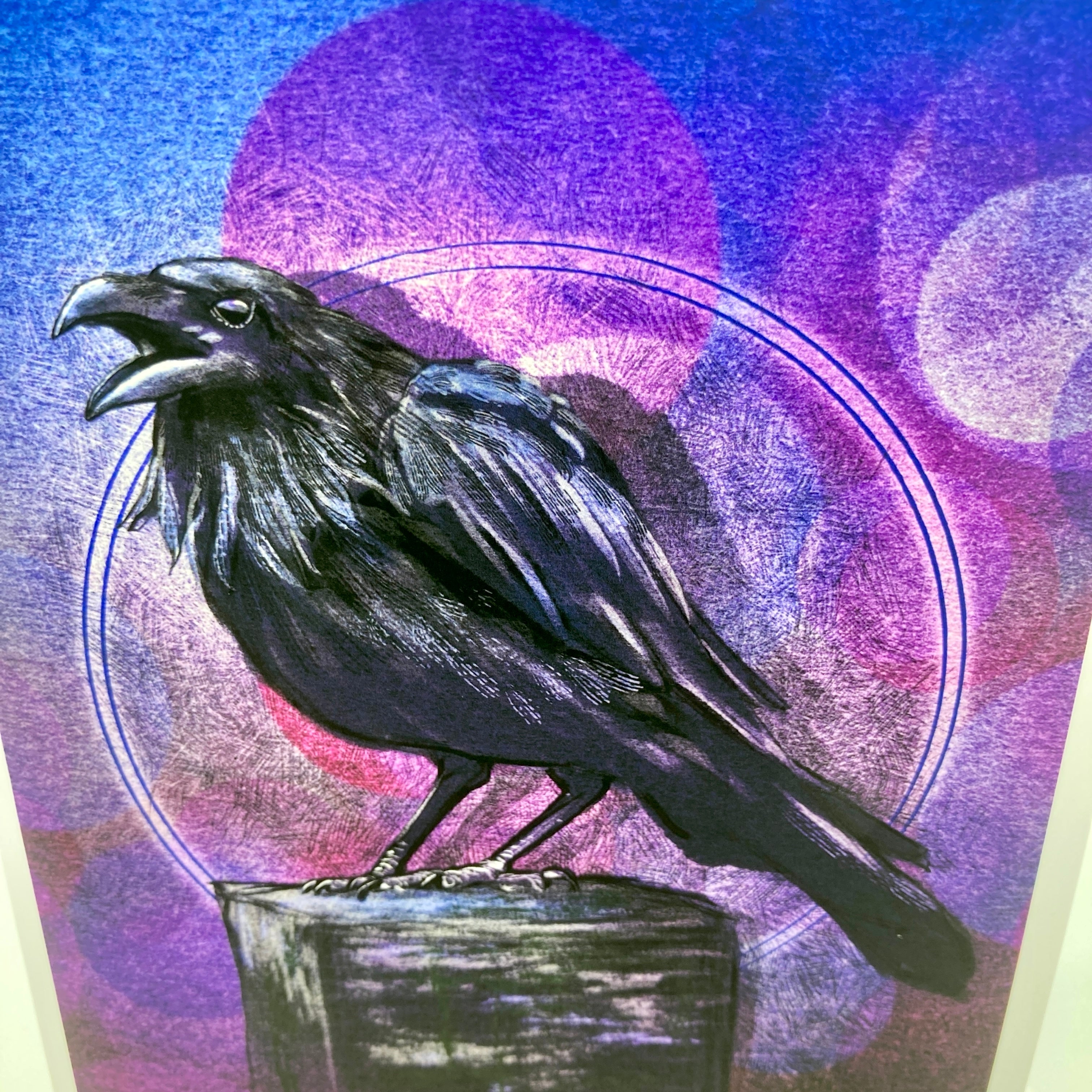 A square art print or card featuring a detailed black raven perched on a dark pedestal, set against a textured background of purple, blue, and pink circular moon phases.