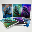 A set of raven-themed art prints and cards displayed on a light gray background. The prints feature painted ravens perched on branches against colorful abstract backgrounds with blue, green, purple, and brown tones, and one card shows a black raven in profile.