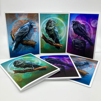 A set of raven-themed art prints and cards displayed on a light gray background. The prints feature painted ravens perched on branches against colorful abstract backgrounds with blue, green, purple, and brown tones, and one card shows a black raven in profile.