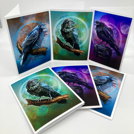 Six illustrated raven art cards or prints fanned out on a white surface, each showing a black bird perched on a branch within circular mystical designs and colorful blue, green, and purple backgrounds.