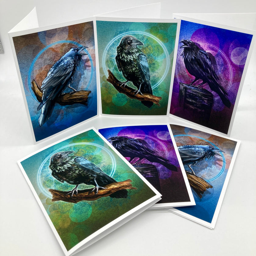 Six illustrated raven art cards or prints fanned out on a white surface, each showing a black bird perched on a branch within circular mystical designs and colorful blue, green, and purple backgrounds.