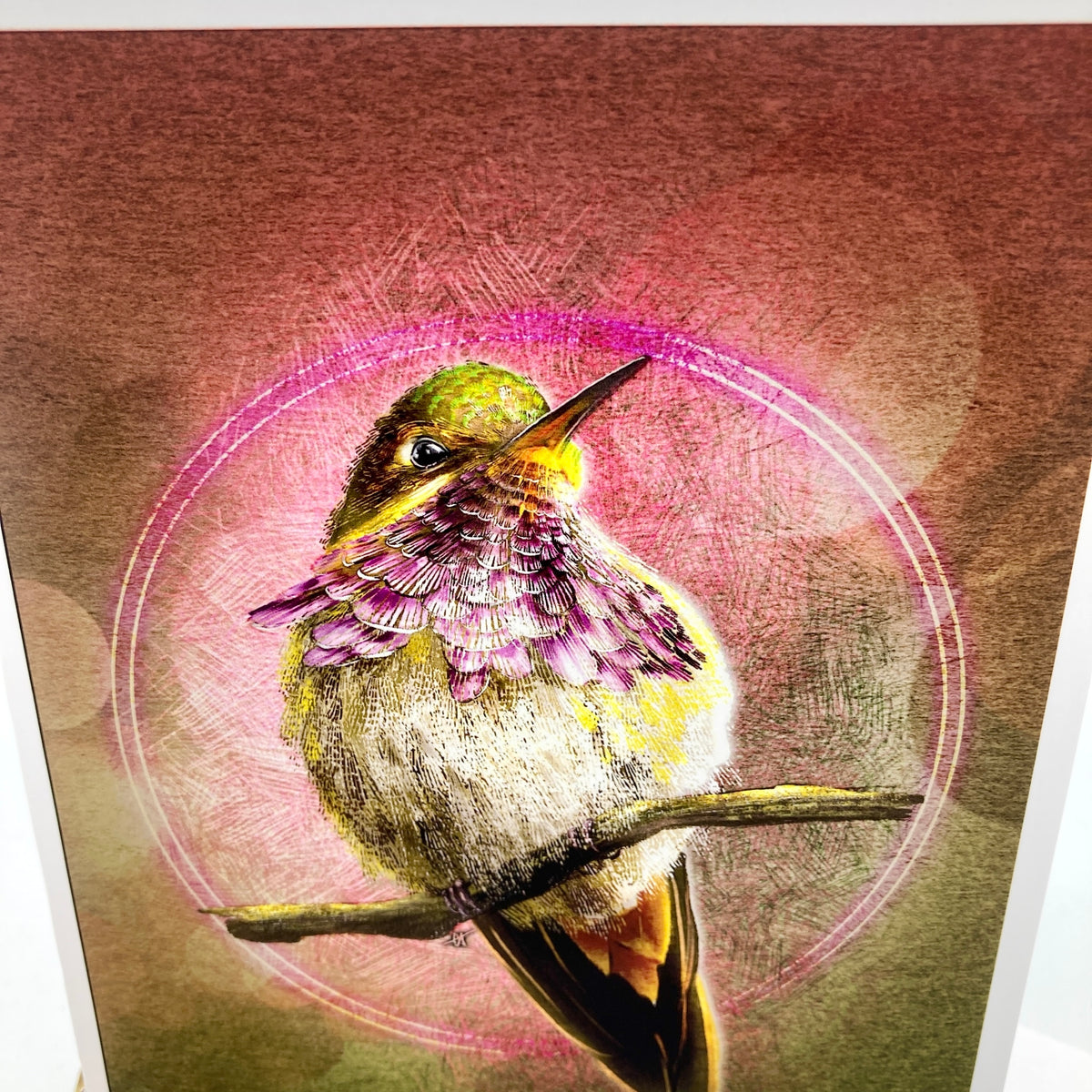 A close-up of a textured art print or painting depicting a hummingbird perched on a branch, with a pink circular glow and brushstroke background.