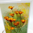 A square art print or card featuring a cluster of orange poppy flowers with green stems on a textured light green and yellow background, photographed standing against a white surface.