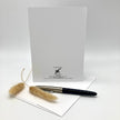 A white stationery card set with a black printed logo for 'Bad Tired Print' and 'The Art of Lettering', styled with a black and silver pen and dried pampas grass on a white envelope against a white background.
