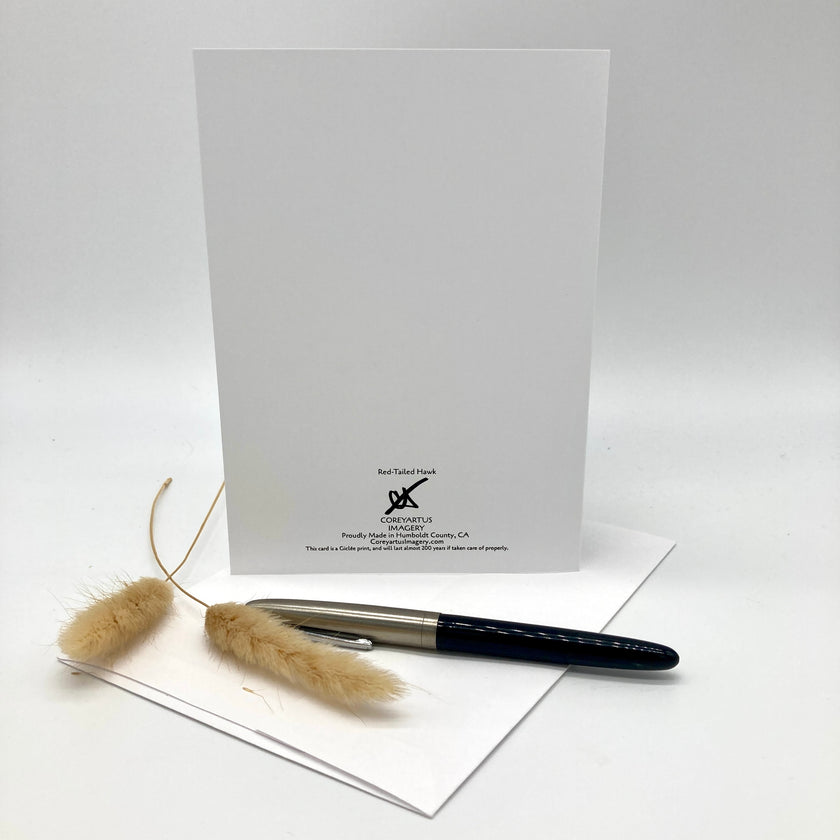 A white stationery card set with a black printed logo for 'Bad Tired Print' and 'The Art of Lettering', styled with a black and silver pen and dried pampas grass on a white envelope against a white background.
