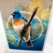 A card featuring a detailed illustration of a bluebird perched on a branch, with a textured abstract background in blue, gold, and gray tones.