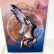 A card featuring a stylized eagle in flight with wings spread, set against an abstract background of purple, pink, and blue tones with circular linework. The print is photographed standing upright against a white background.