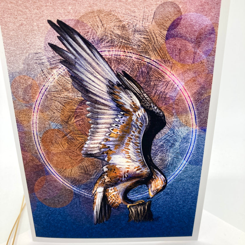 A card featuring a stylized eagle in flight with wings spread, set against an abstract background of purple, pink, and blue tones with circular linework. The print is photographed standing upright against a white background.