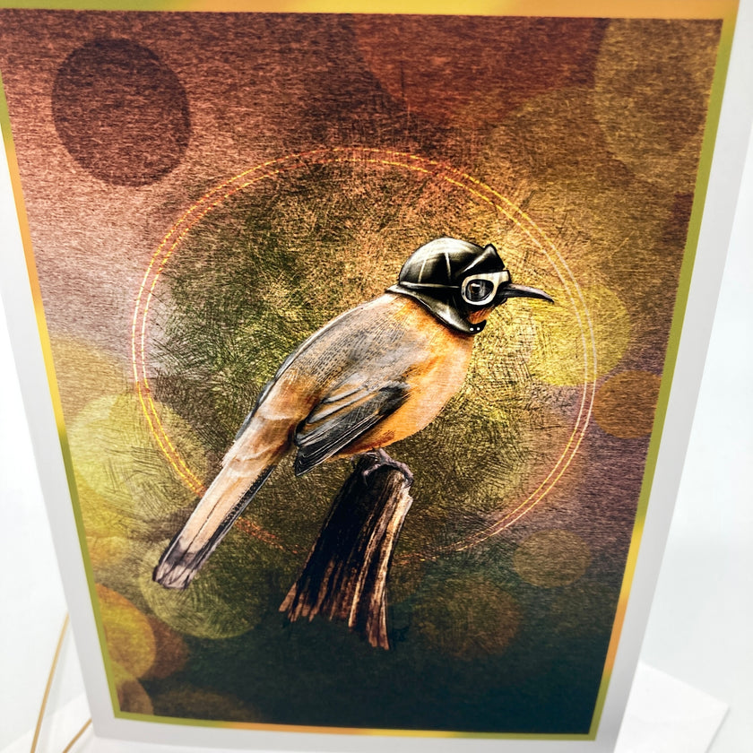 An art print or card featuring a bird wearing a small black helmet and goggles, perched on a branch against a textured abstract background with warm brown, gold, and olive tones. The print is photographed at a slight angle with a white border visible around the artwork.