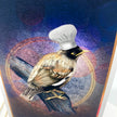A close-up of a colorful art print or card featuring a bird perched on a branch, wearing a white chef's hat, against a blue and purple abstract background.