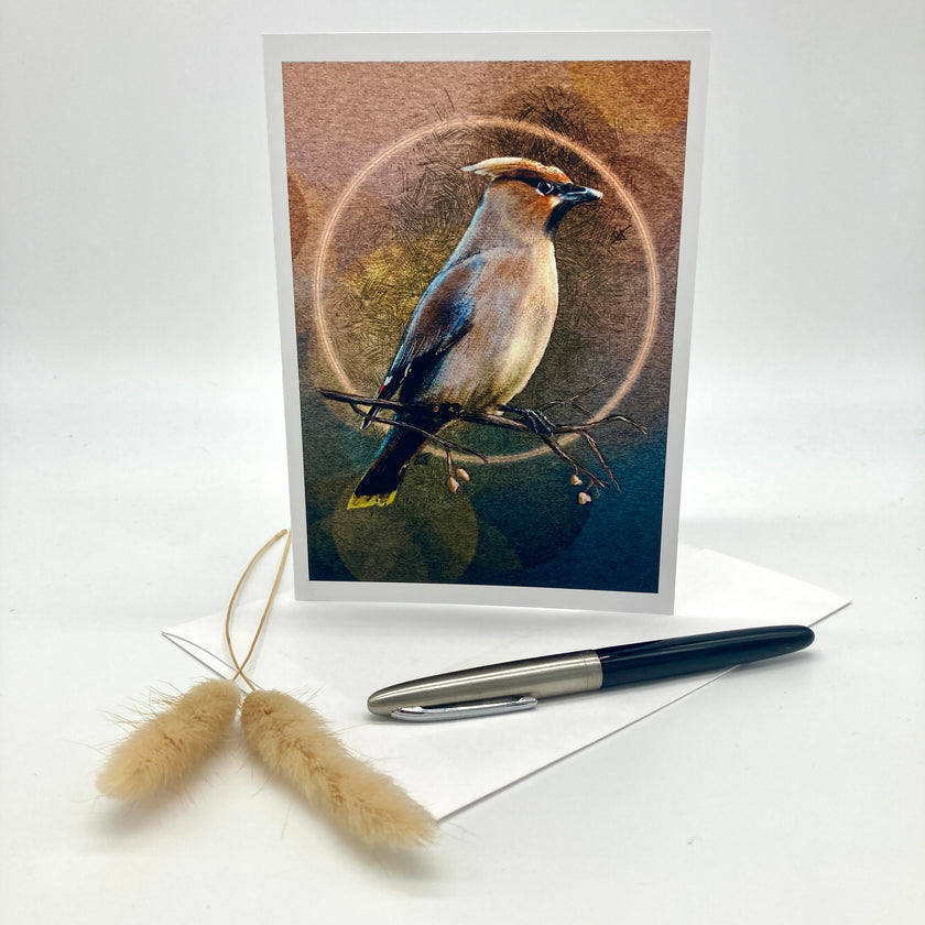 A vertical art print or greeting card featuring a detailed bird illustration with a circular halo motif, displayed upright on a white surface with an envelope, a black pen, and two dried bunny tail stems.