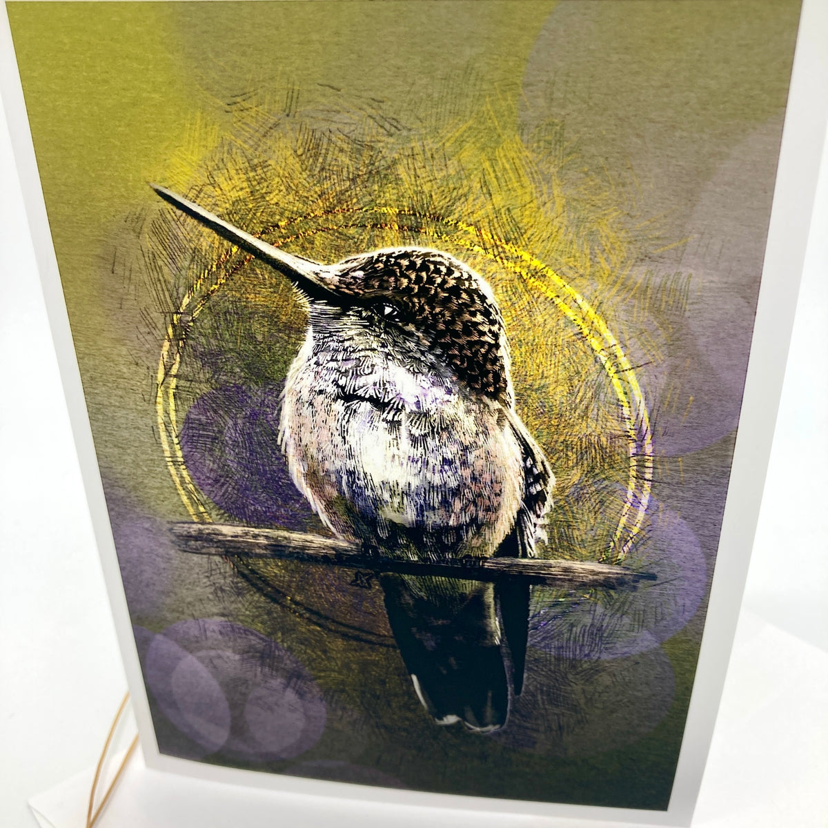 A close up of a greeting card featuring a detailed hummingbird perched on a branch, set against an abstract textured background with yellow, olive green, and purple tones.
