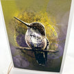 A close up of a greeting card featuring a detailed hummingbird perched on a branch, set against an abstract textured background with yellow, olive green, and purple tones.