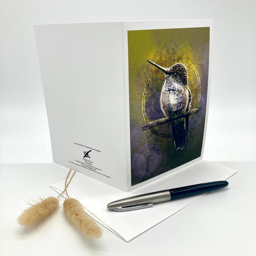 A white greeting card standing upright on a white surface, featuring a printed illustration of a bird perched against a yellow-green and purple textured background. A white envelope lies beneath a black and silver pen, with two small dried grass stems on the left.