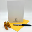 The back of a white greeting card posed on a yellow envelope with berries and an ink pen as props.