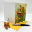 A spalyed out stylized floral greeting card showing a cluster of orange poppy-like flowers with green stems on a textured pale green background with soft yellow bokeh circles and a faint circular line motif. Posed with a yellow envelope.
