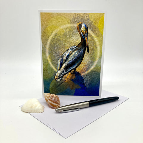 Illustrated greeting card featuring a California Brown Pelican on a stylized textured background of gold and blue, posed on a white envelope with two shells and an ink pen against a brown paper background.