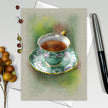 Card with a green teacup and saucer illustration on a textured surface.