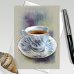 Greeting card with a painting of a teacup and saucer on a textured surface.
