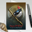 Birthday card with a bird wearing a party hat on a branch, with a pen and shell in the background.