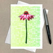 Greeting card with pink flower design on a green polka dot background, placed on a brown surface with a pen.