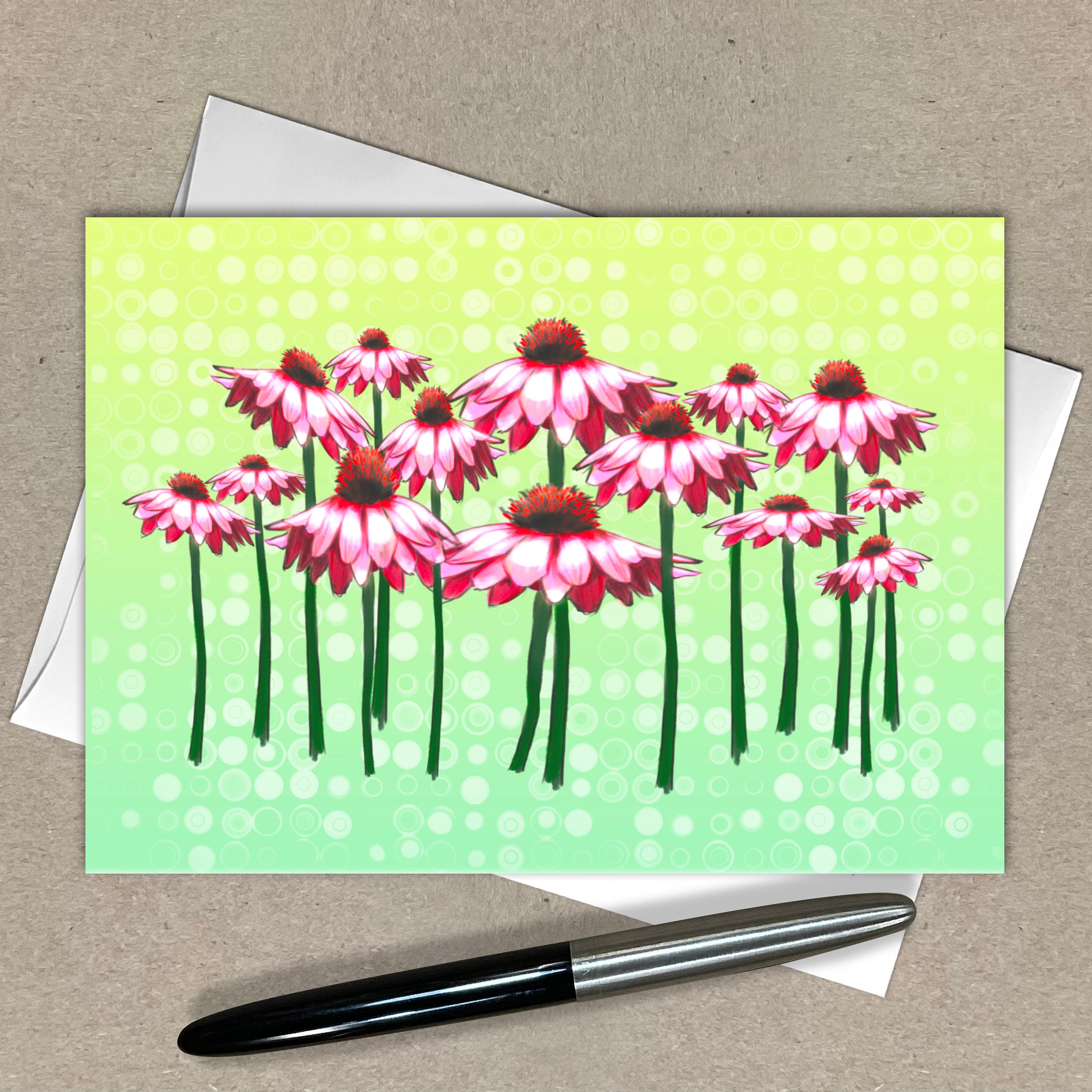 Greeting card with pink flowers on a green background, pen and envelope on a beige surface