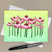 Greeting card with pink flowers on a green background, pen and envelope on a beige surface