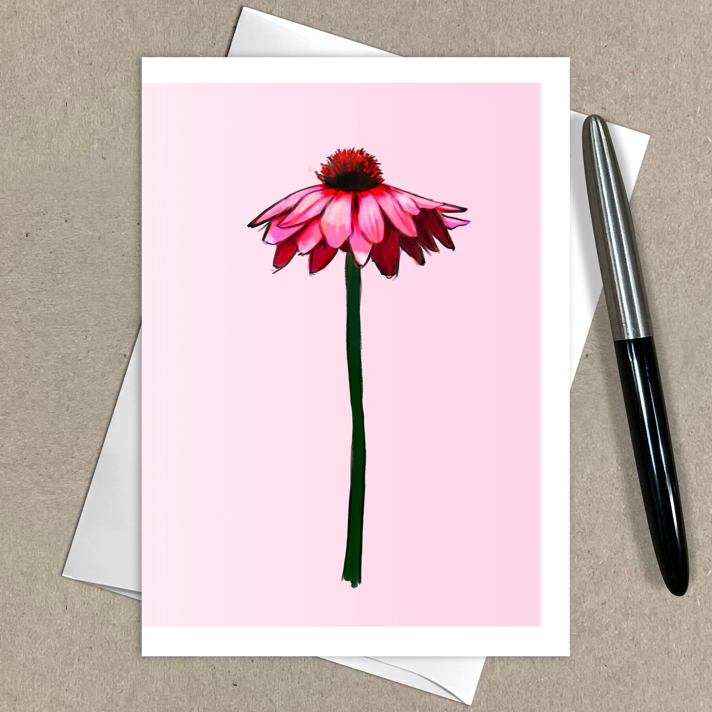 Greeting card with a pink flower illustration on a pink background, placed on a brown surface with a pen.