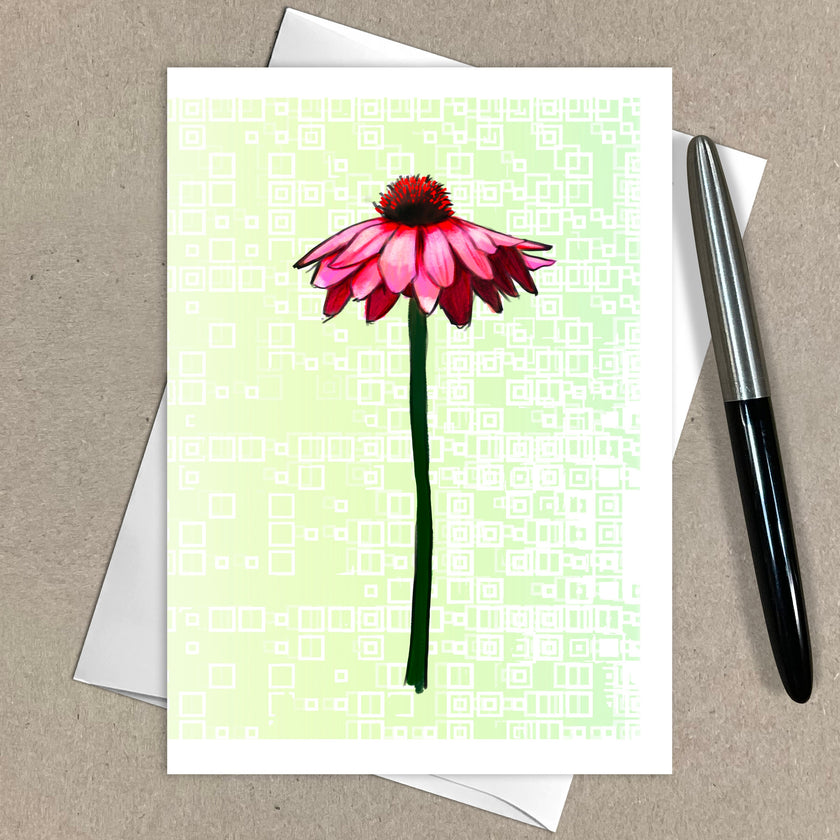 Greeting card with a pink flower design on a light green background, placed on a brown surface with an envelope and pen.