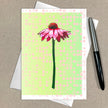 Greeting card with pink flower design on a green polka dot background, with an envelope and pen on a brown surface.