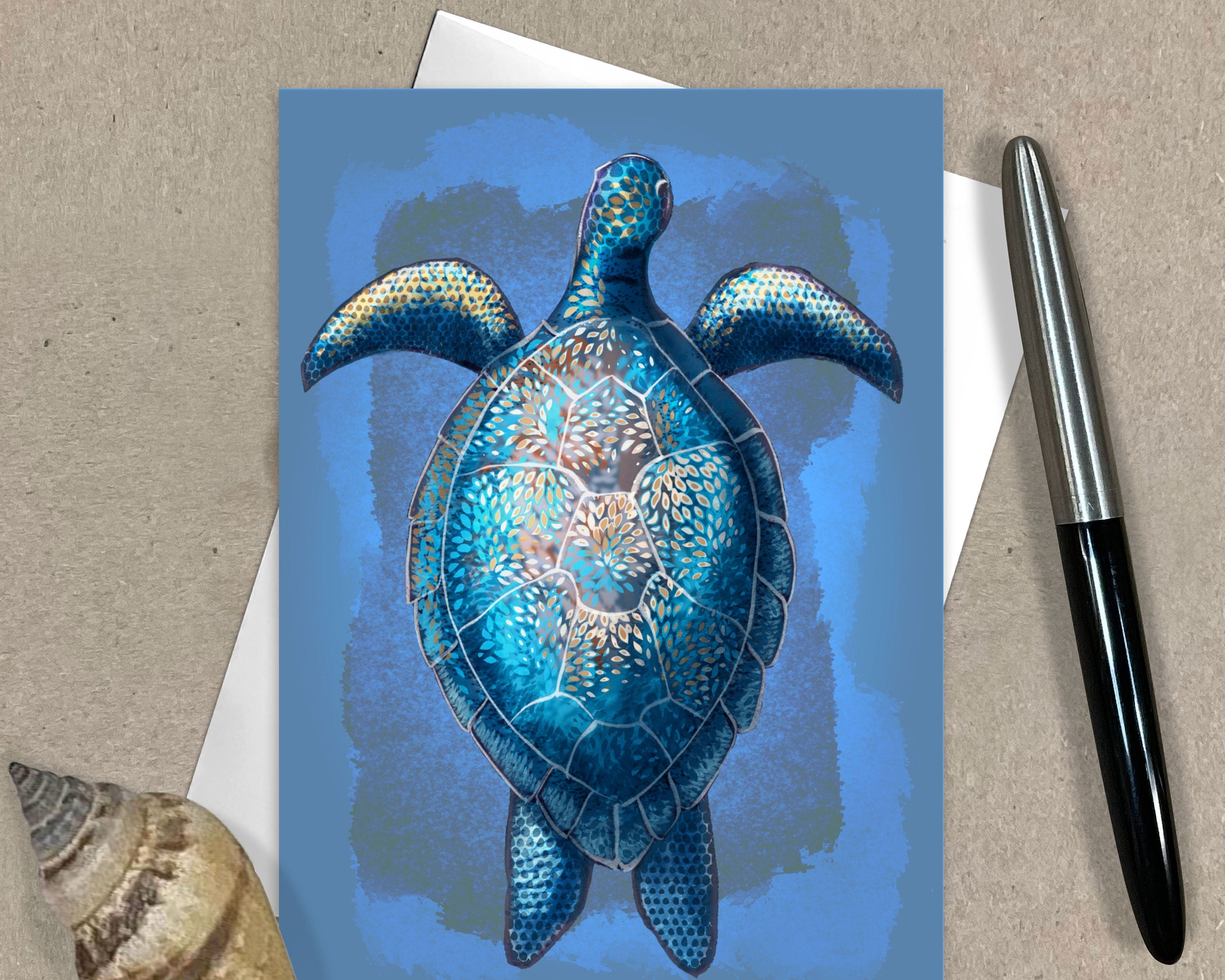 Greeting card with a blue turtle design on a textured surface with a pen and shell.