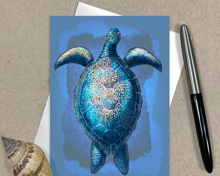 Greeting card with a blue turtle design on a textured surface with a pen and shell.