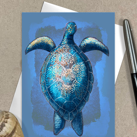 Greeting card with a blue turtle design on a textured surface with a pen and shell.