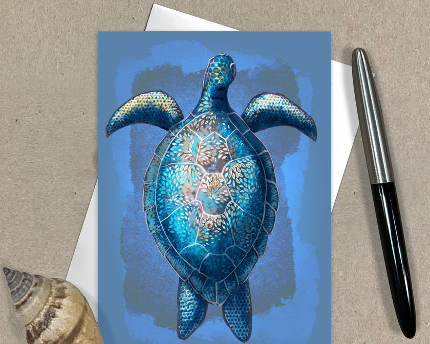Greeting card with a blue turtle design on a textured surface with a pen and shell.