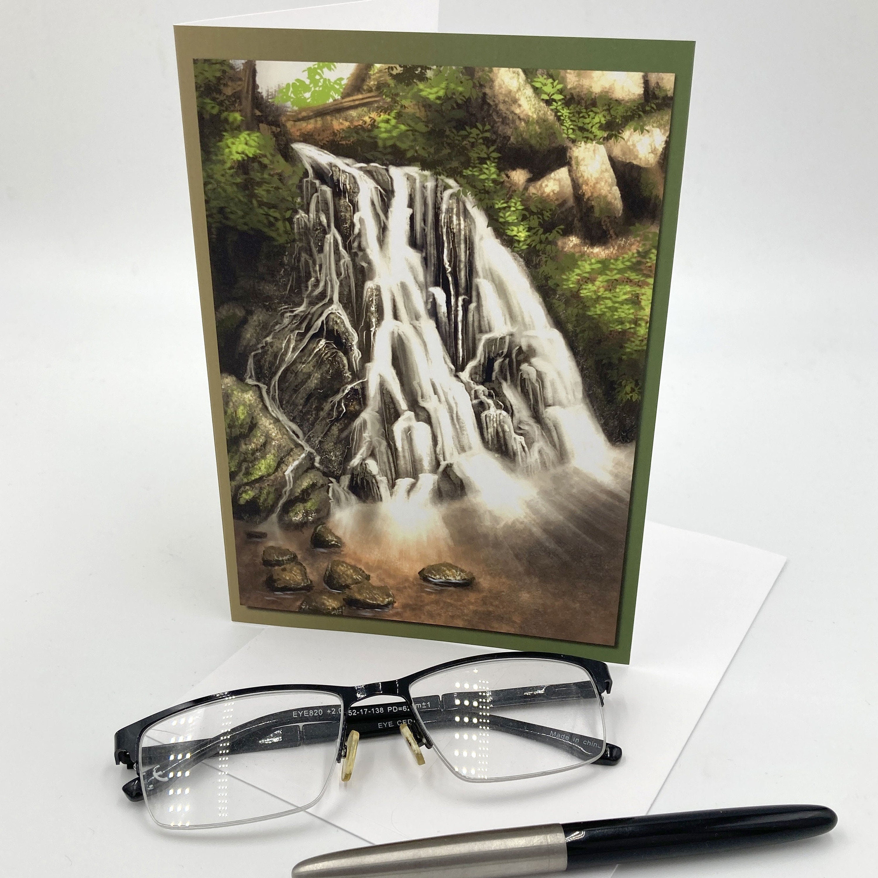 Greeting card with a waterfall design, glasses, and a pen on a white background