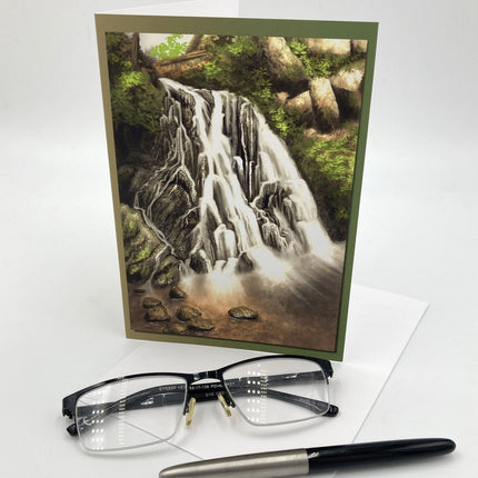 Greeting card with a waterfall design, glasses, and a pen on a white background