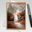 Greeting card with a watercolor painting of a forest scene with a waterfall, pen on the side.