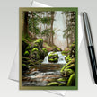 Greeting card with a forest scene featuring a stream and waterfall, with a pen on the side.