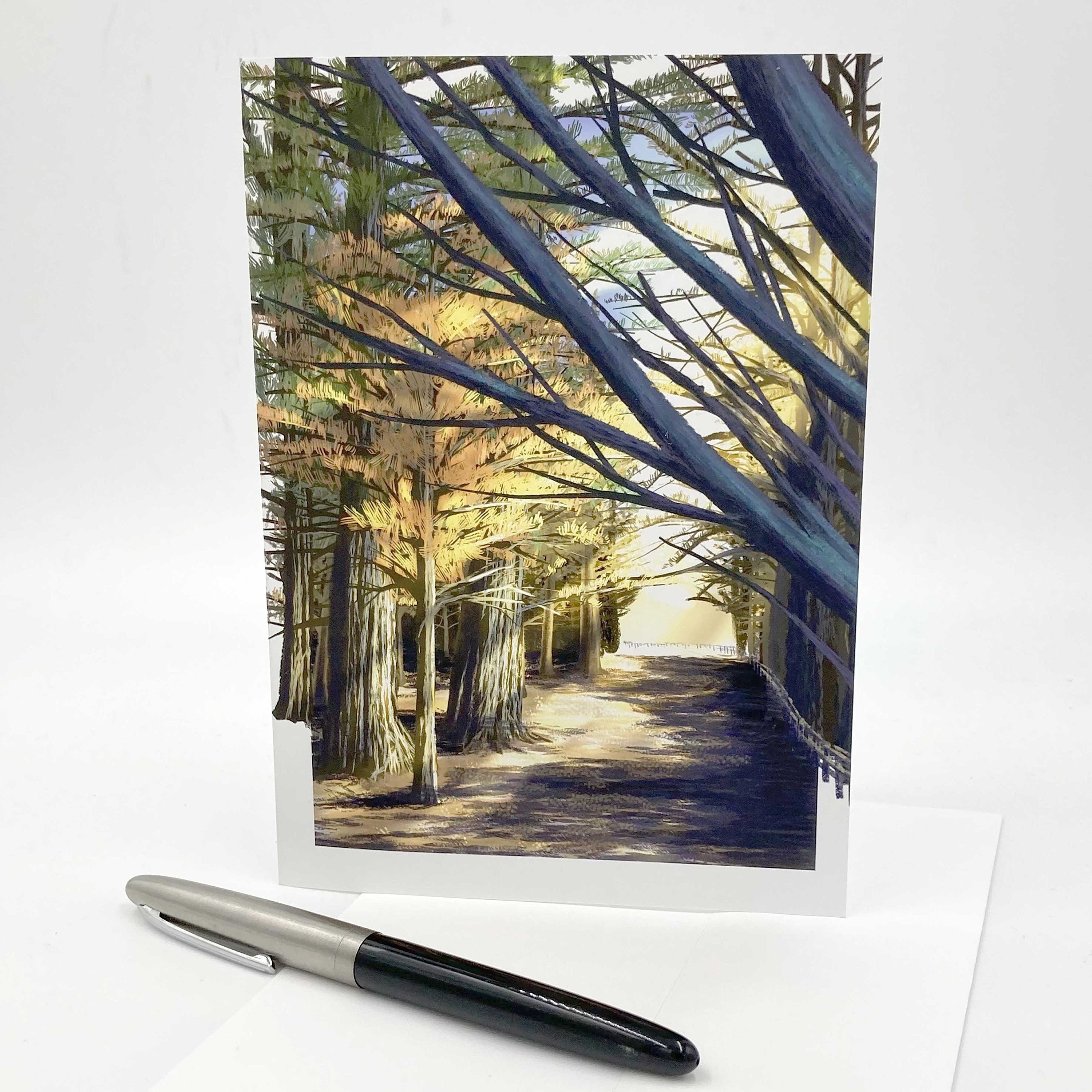 Greeting card with a scenic view of a tree-lined path and a pen on a white background