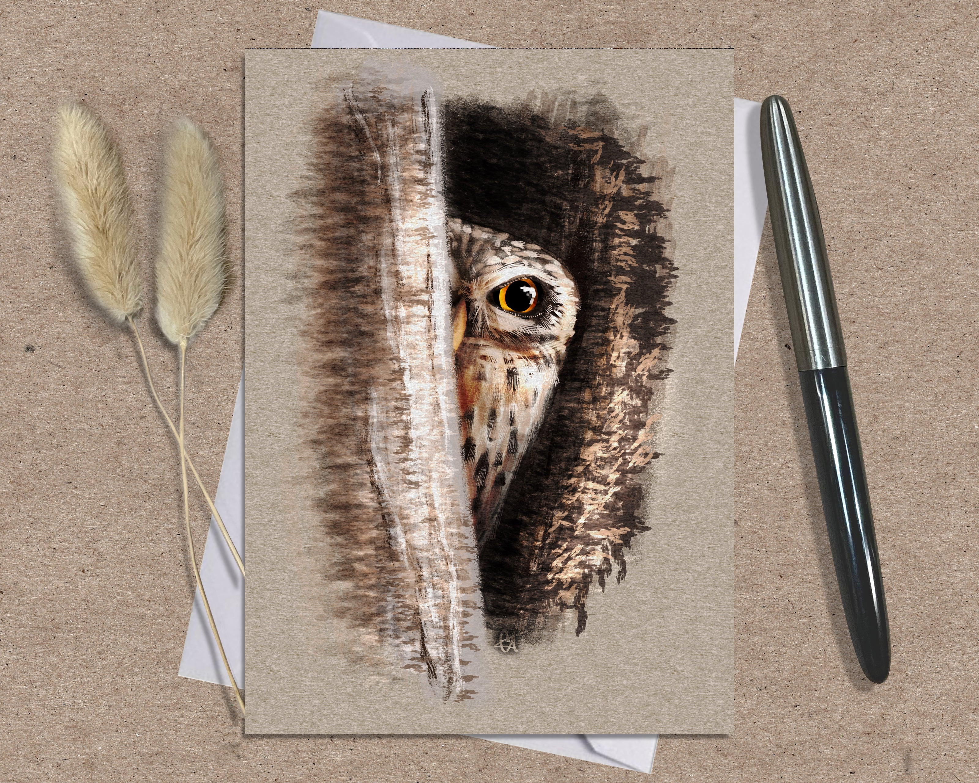 Greeting card with owl illustration on a textured surface with a pen and dried plants.