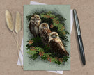 Greeting card with owls design on a textured surface with a pen and dried plants.