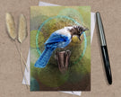 Greeting card with a blue bird design on a textured surface with a pen and dried plants.
