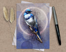 Greeting card with a blue bird illustration on a textured surface with a pen and dried plants.